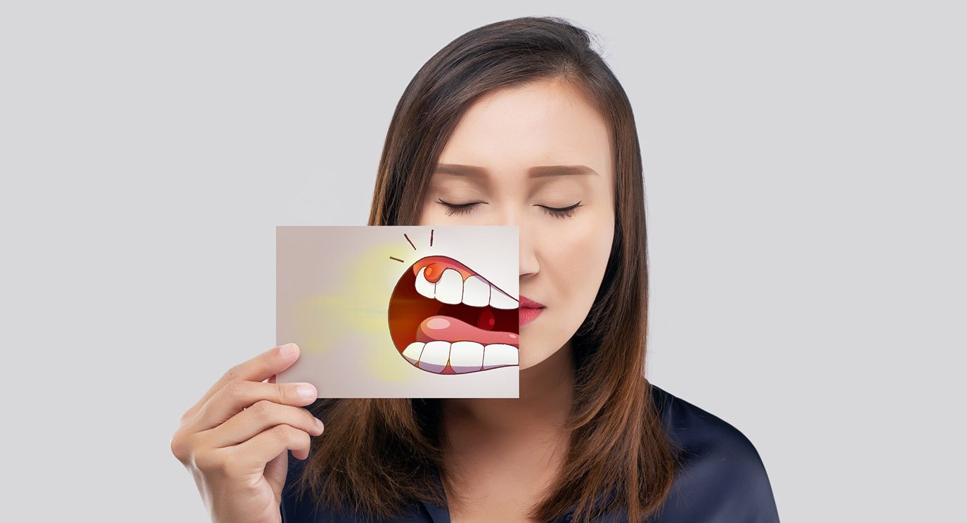 Young person with eyes closed holding a drawing of cartoon gum cancer in front of her mouth