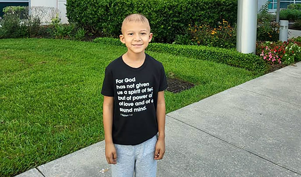 Christian Garcia standing in front of the MD Anderson Proton Therapy Center. He is smiling while wearing a black t-shirt, with his arms by his sides.