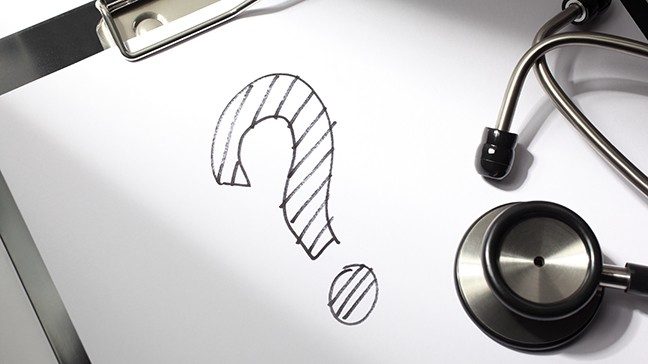A stethoscope lies on a white sheet of paper that has a question mark drawn on it